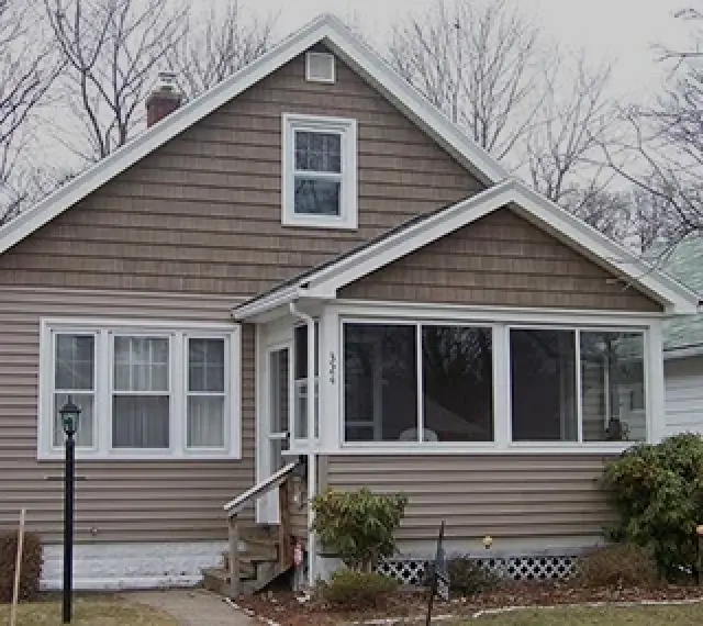 A small brown house with a screened front porch and bare trees in the background.