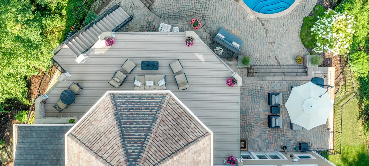 An aerial view of a home's exterior, including the roof, deck, patio, stairs, and pool.