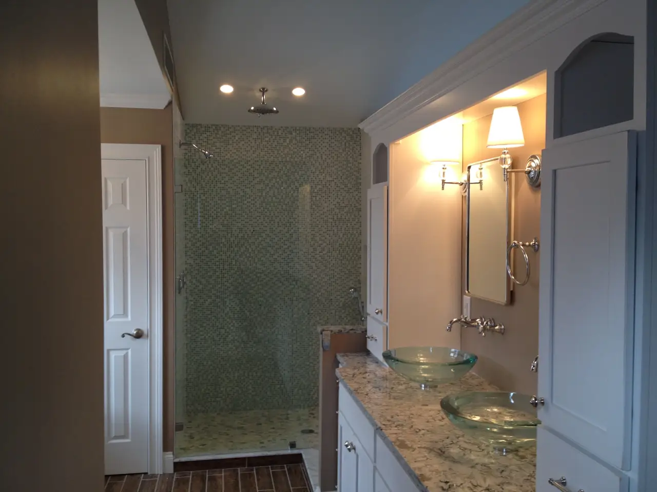 A modern bathroom featuring a glass shower, dual sinks with glass bowls, and stylish lighting.
