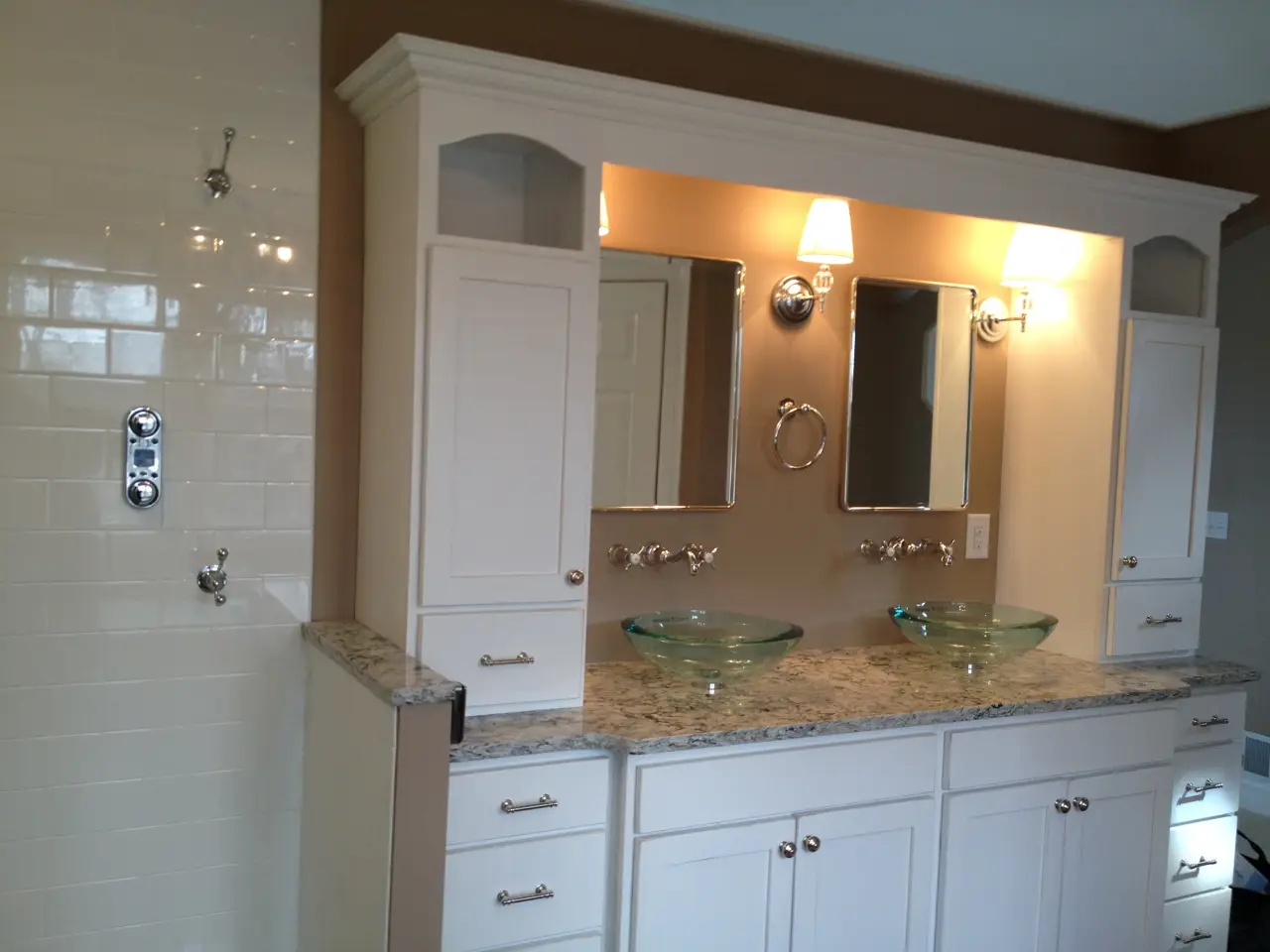 A modern bathroom with a double vanity, two mirrors, glass sinks, and a tiled shower area. Soft lighting enhances the space.