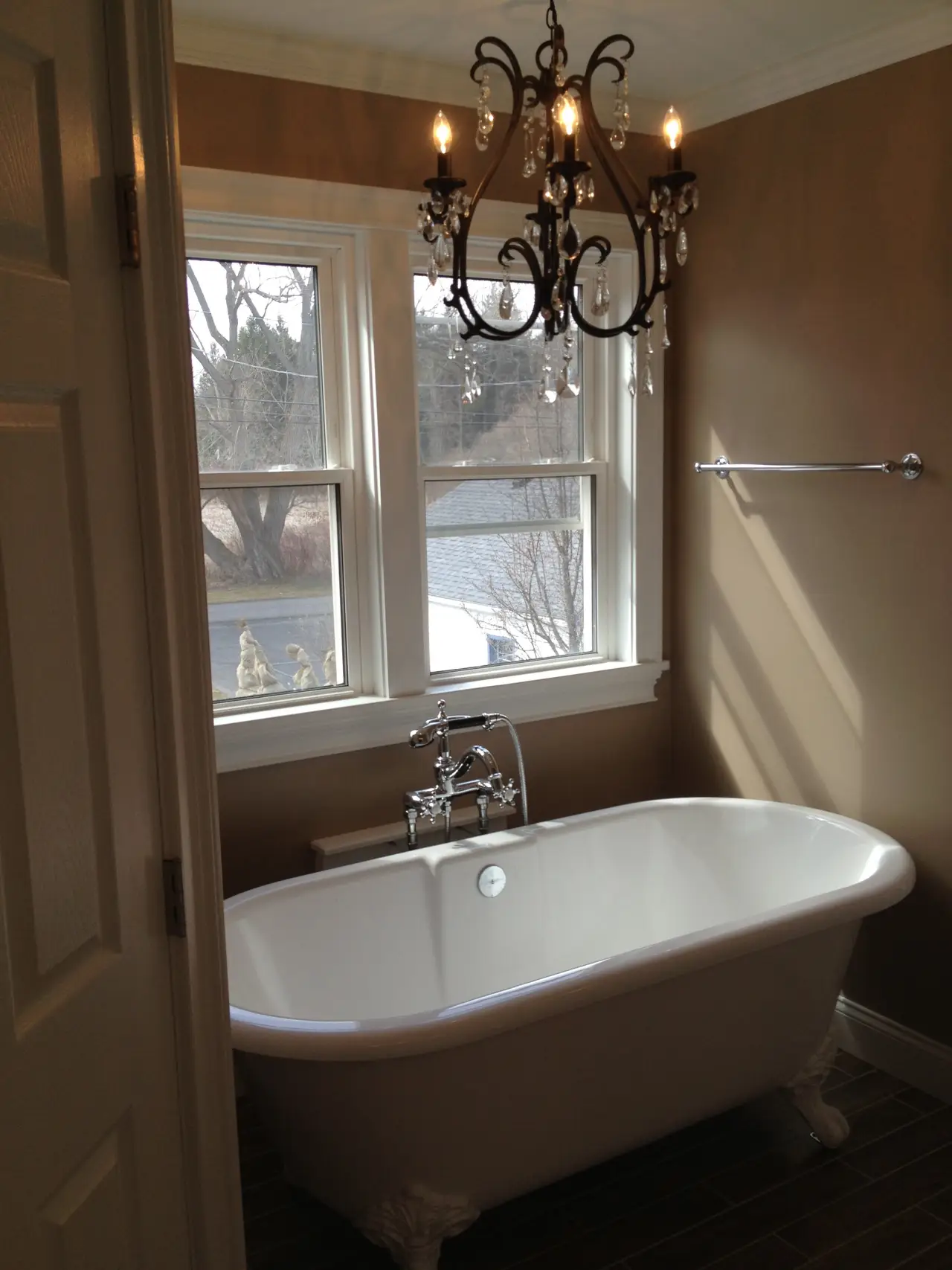 A stylish bathroom featuring a freestanding bathtub, elegant chandelier, and large windows with natural light.