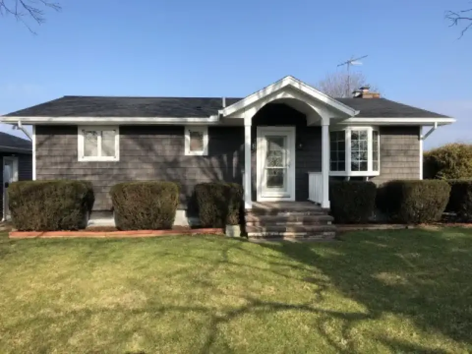Single-story house with gray siding, white trim, front porch, shrubs, and a grassy yard.