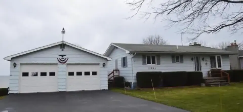 Light blue ranch house with attached garage, paved driveway, and green lawn on a cloudy day.