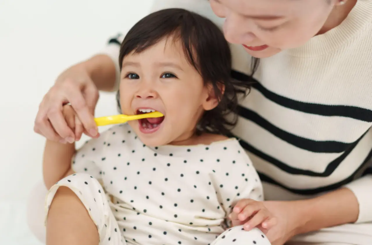 A toddler brushes their teeth with help from an adult.