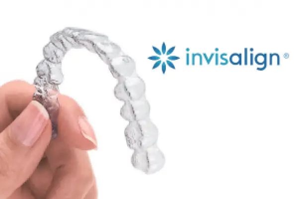 Hand holding a clear aligner; Invisalign logo is visible in the background.