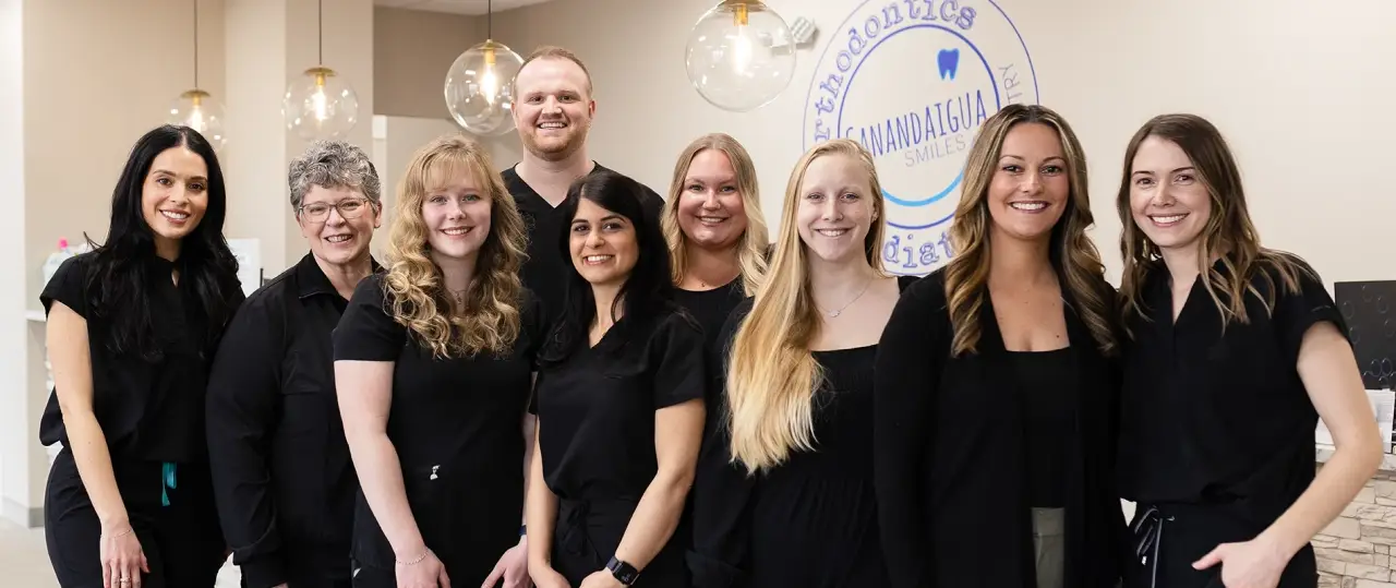 The Canandaigua Smiles team in black outfits smiling inside a modern orthodontic office.