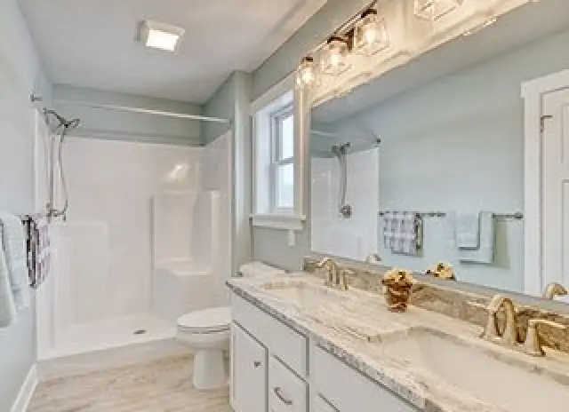 bright bathroom with soft blue walls, marble counters, gold accents