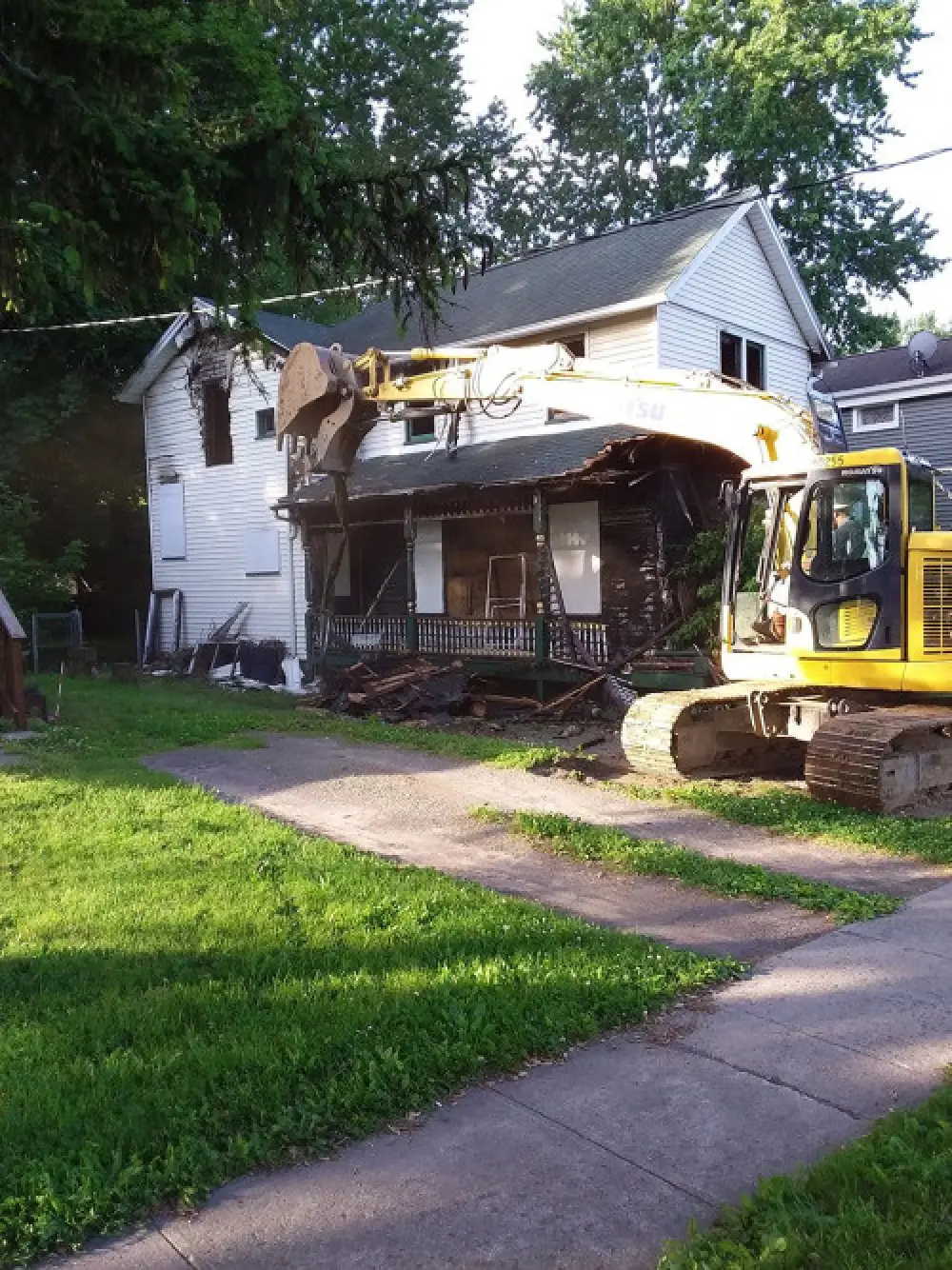 A Sortino Properties demolition team member demolishing a white house with a backhoe.