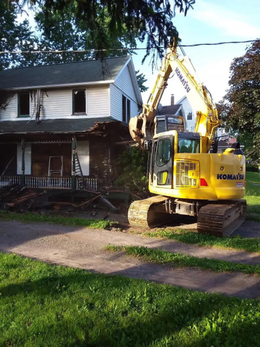 A backhoe sitting in front of a white house being demolished.