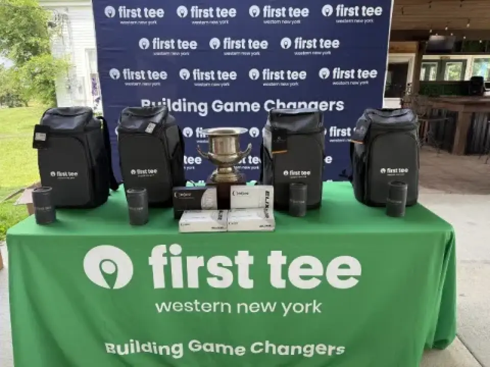 Golf prizes, bags, and a trophy displayed on a table with first tee western New York branding.