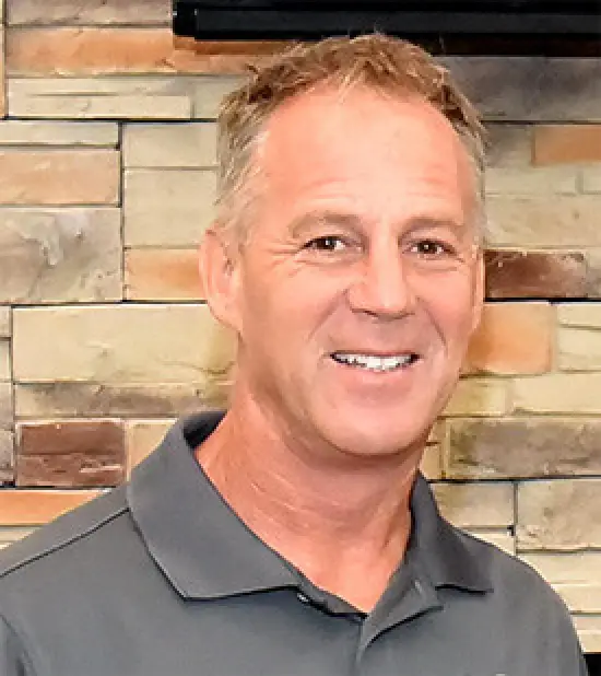 Peter Bruckel president and managing member at Quicklees in a gray polo shirt standing in front of a brick wall background.