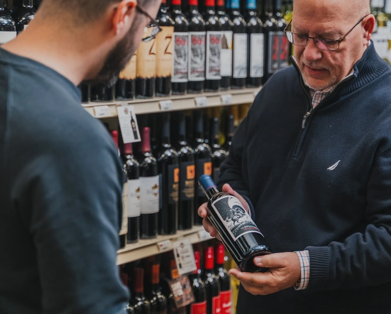 older man store worker shows customer bottle of wine